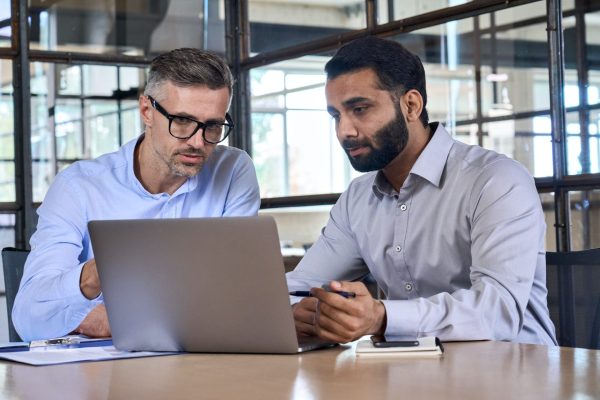 Two business men analysts discussing data management using laptop computer.